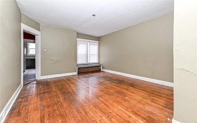 spare room featuring hardwood / wood-style floors, radiator, and a healthy amount of sunlight