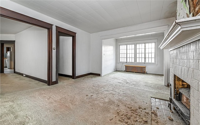 unfurnished living room featuring a fireplace, radiator heating unit, and light colored carpet