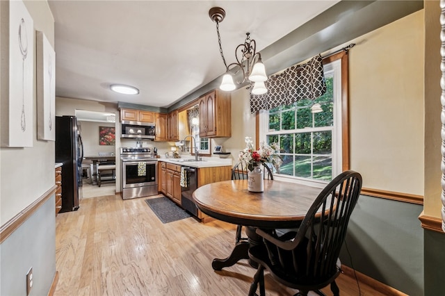 kitchen with a notable chandelier, light wood-type flooring, black appliances, and decorative light fixtures