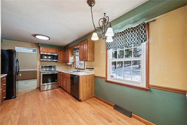 kitchen featuring decorative light fixtures, sink, light wood-type flooring, and black appliances