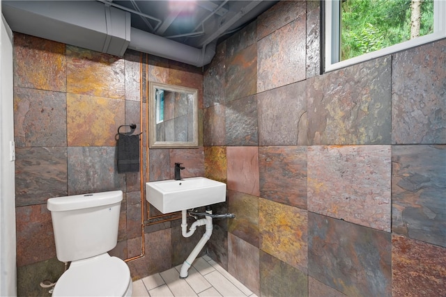 bathroom with toilet, tile patterned floors, and tile walls