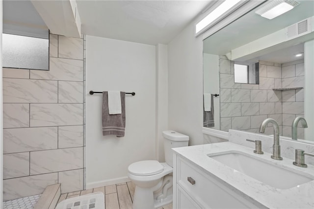 bathroom featuring toilet, a tile shower, tile patterned flooring, and vanity