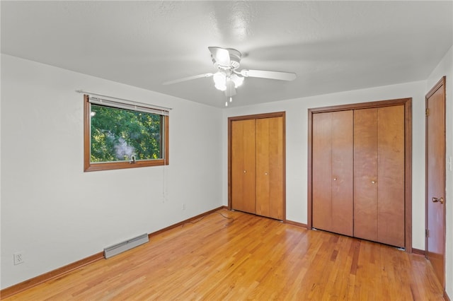 unfurnished bedroom with a baseboard heating unit, ceiling fan, multiple closets, and light hardwood / wood-style floors