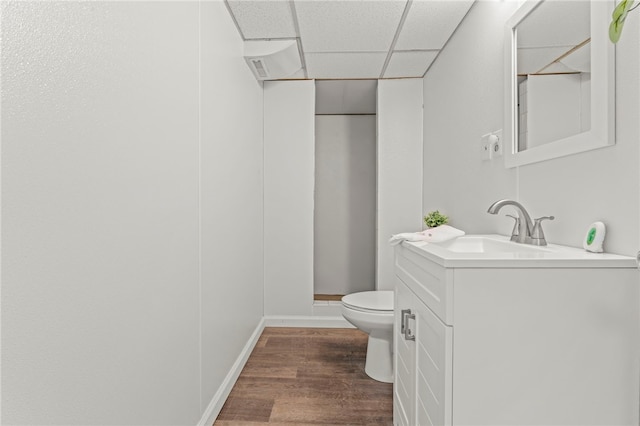 bathroom with wood-type flooring, a paneled ceiling, vanity, and toilet