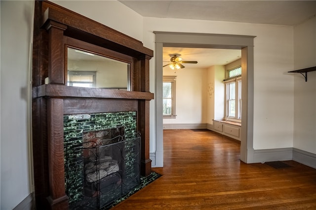 unfurnished living room featuring ceiling fan, a tiled fireplace, and wood-type flooring