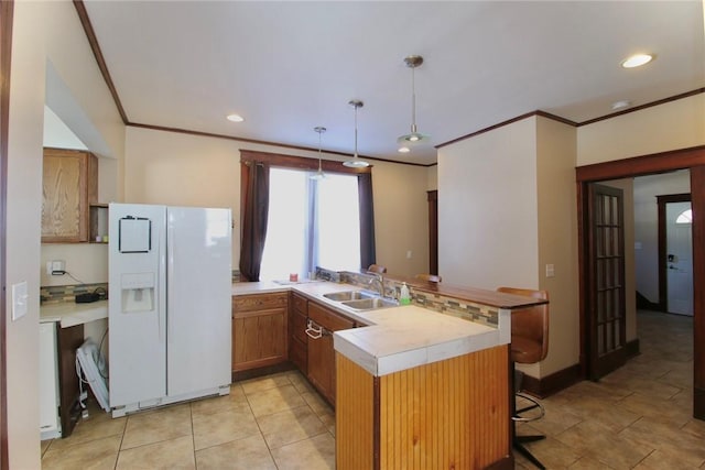 kitchen featuring sink, a breakfast bar area, hanging light fixtures, white fridge with ice dispenser, and kitchen peninsula