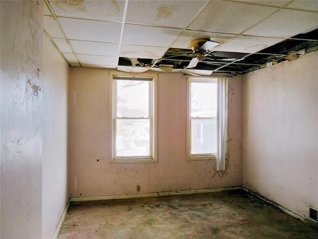 empty room with a paneled ceiling, plenty of natural light, and concrete flooring