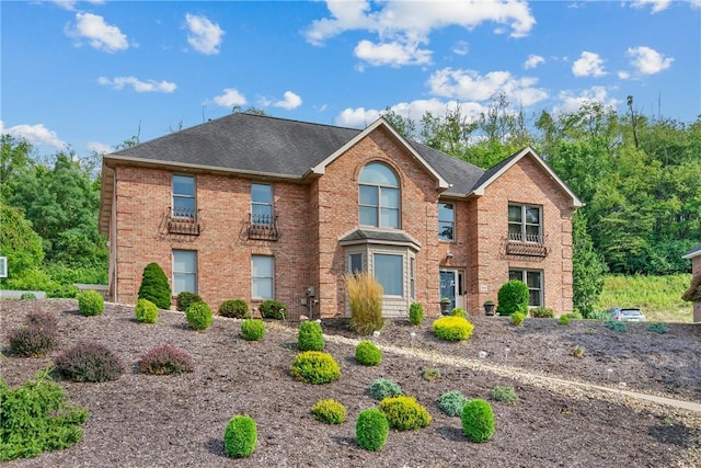 colonial-style house with roof with shingles and brick siding