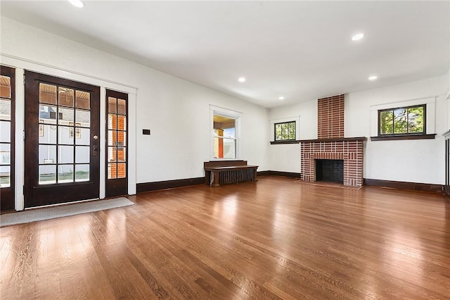 unfurnished living room with a healthy amount of sunlight, a brick fireplace, wood finished floors, and recessed lighting