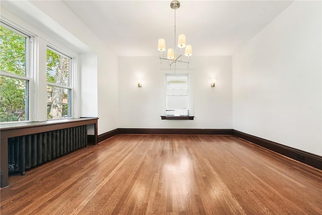 spare room featuring baseboards, an inviting chandelier, wood finished floors, and radiator