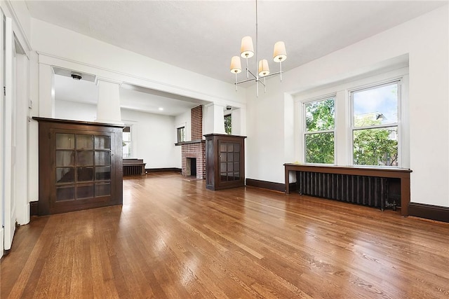 interior space with radiator, a brick fireplace, baseboards, and wood finished floors