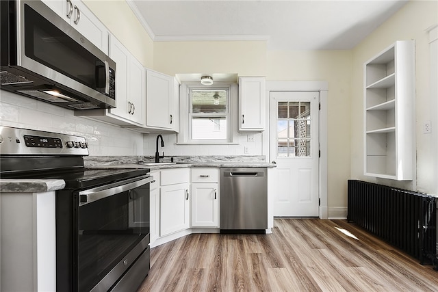 kitchen with appliances with stainless steel finishes, white cabinets, radiator, sink, and light hardwood / wood-style floors