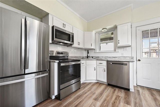 kitchen featuring light stone counters, a sink, white cabinets, ornamental molding, and appliances with stainless steel finishes