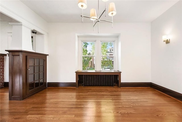 unfurnished dining area featuring a chandelier, radiator heating unit, wood finished floors, and baseboards