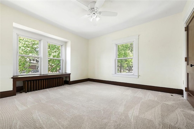 empty room with radiator, light carpet, baseboards, and a ceiling fan