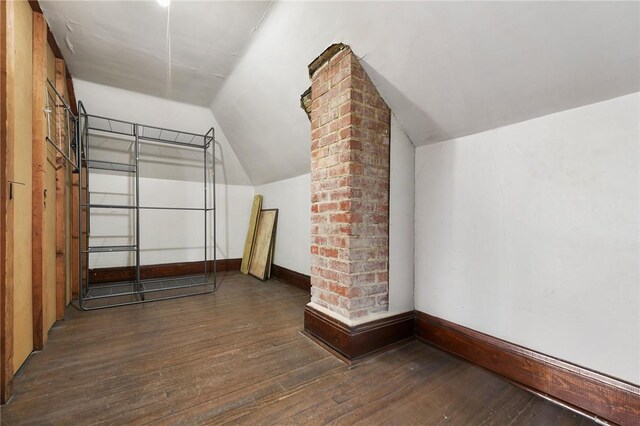 bonus room with lofted ceiling, dark hardwood / wood-style flooring, and brick wall