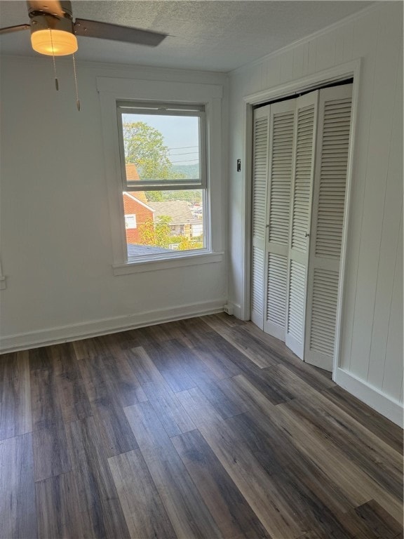 unfurnished bedroom featuring ceiling fan, a textured ceiling, a closet, and dark hardwood / wood-style flooring