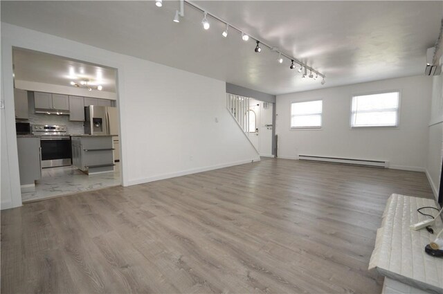 unfurnished living room with rail lighting, a baseboard radiator, and light wood-type flooring