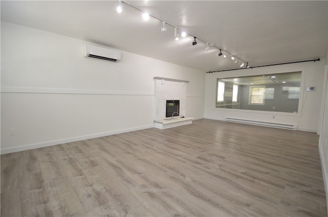 unfurnished living room with a baseboard radiator, wood-type flooring, a brick fireplace, track lighting, and a wall mounted air conditioner