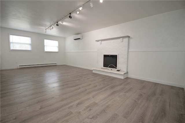 unfurnished living room with baseboard heating, track lighting, wood-type flooring, and a brick fireplace