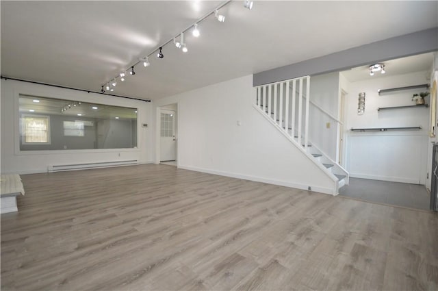 unfurnished living room with a baseboard radiator, wood finished floors, baseboards, stairs, and rail lighting