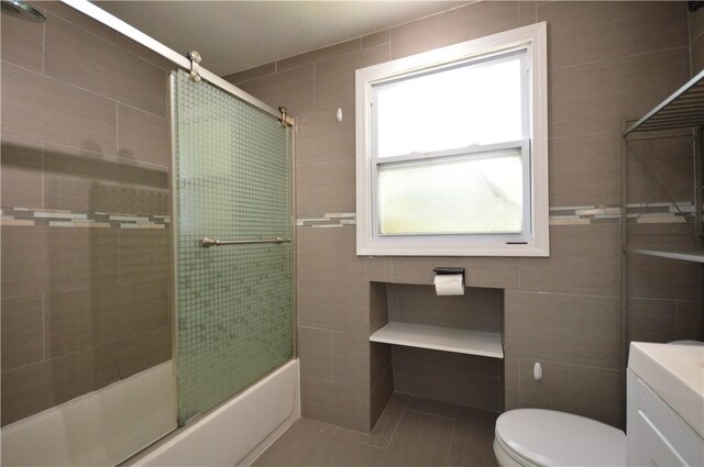 full bathroom featuring toilet, tile walls, shower / bath combination with glass door, tile patterned flooring, and vanity