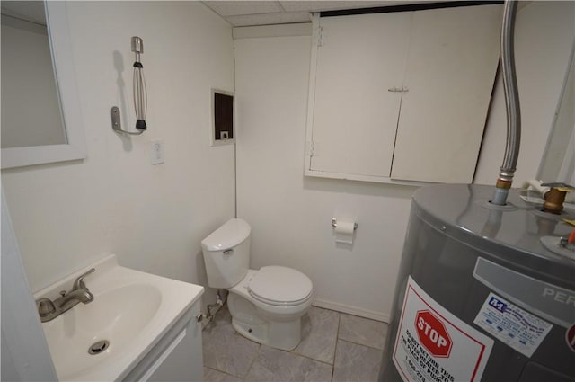 bathroom featuring a drop ceiling, toilet, vanity, baseboards, and water heater