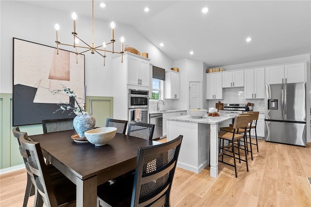 dining space with high vaulted ceiling, an inviting chandelier, sink, and light wood-type flooring