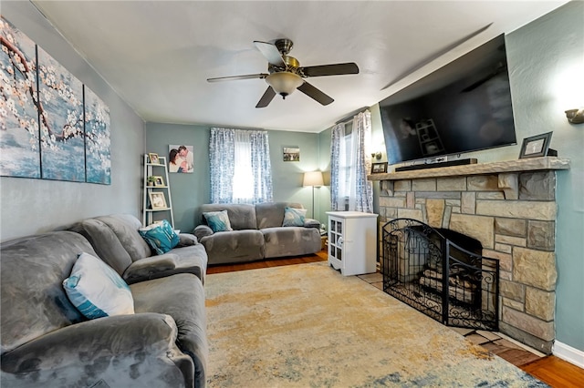 living room featuring ceiling fan, a stone fireplace, and hardwood / wood-style floors