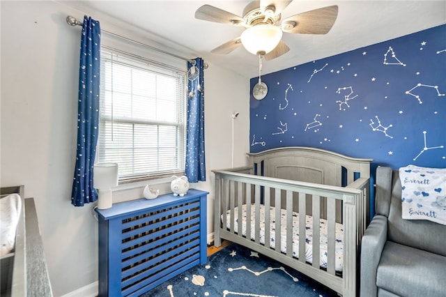 bedroom with a nursery area, carpet flooring, and ceiling fan