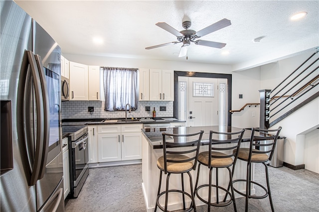 kitchen with decorative backsplash, ceiling fan, appliances with stainless steel finishes, white cabinets, and a center island