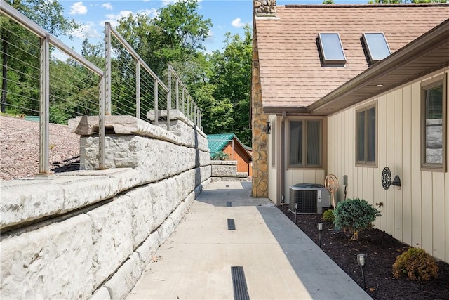 exterior space with a shingled roof, board and batten siding, a patio area, central AC, and a garage