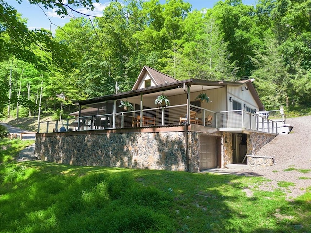 back of house featuring an attached garage, stone siding, a ceiling fan, and a yard