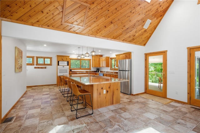 kitchen featuring appliances with stainless steel finishes, a skylight, high vaulted ceiling, a center island, and decorative light fixtures