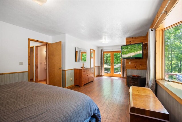 bedroom featuring a textured ceiling, access to outside, wooden walls, french doors, and light hardwood / wood-style flooring