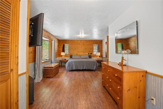 bedroom featuring wooden walls, a textured ceiling, and dark wood-type flooring