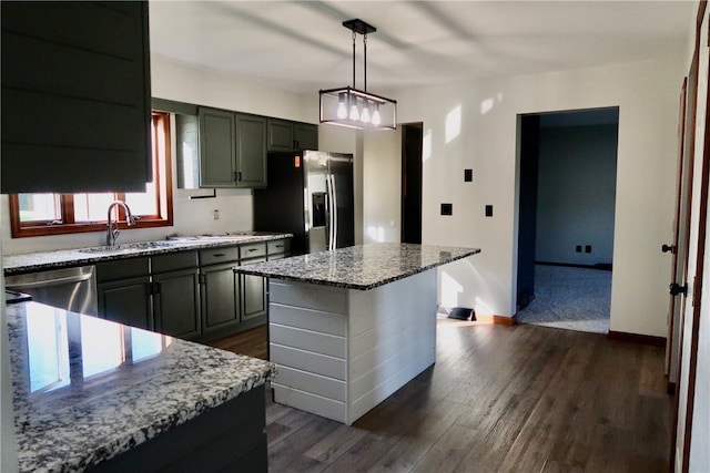 kitchen with a kitchen island, appliances with stainless steel finishes, sink, pendant lighting, and light stone counters