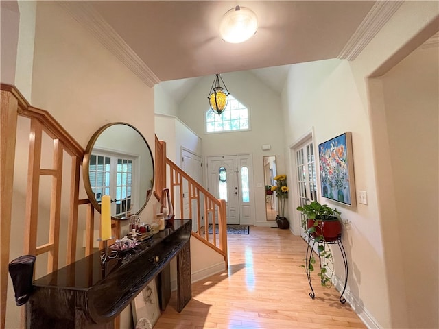 entrance foyer with ornamental molding, a towering ceiling, and light hardwood / wood-style flooring