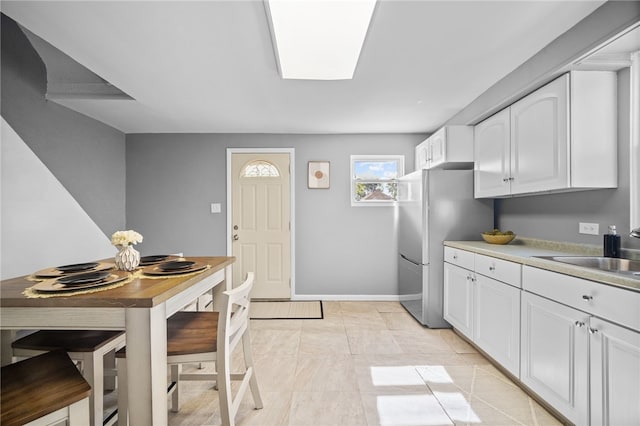 kitchen with white cabinets, sink, light tile patterned floors, and stainless steel refrigerator