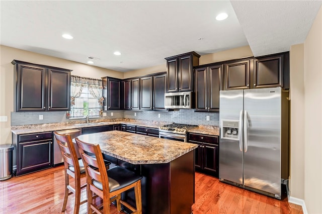 kitchen featuring light wood-type flooring, stainless steel appliances, dark brown cabinets, and a kitchen island