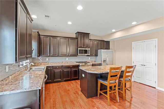 kitchen featuring stainless steel appliances, a center island, light wood-type flooring, tasteful backsplash, and a breakfast bar area