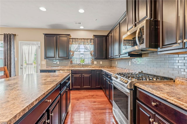 kitchen with backsplash, stainless steel appliances, sink, and light hardwood / wood-style floors