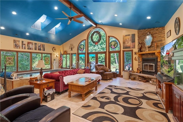 living room with a ceiling fan, high vaulted ceiling, healthy amount of natural light, a skylight, and a stone fireplace