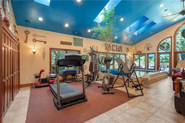 exercise room with high vaulted ceiling, a skylight, light tile patterned floors, and ceiling fan