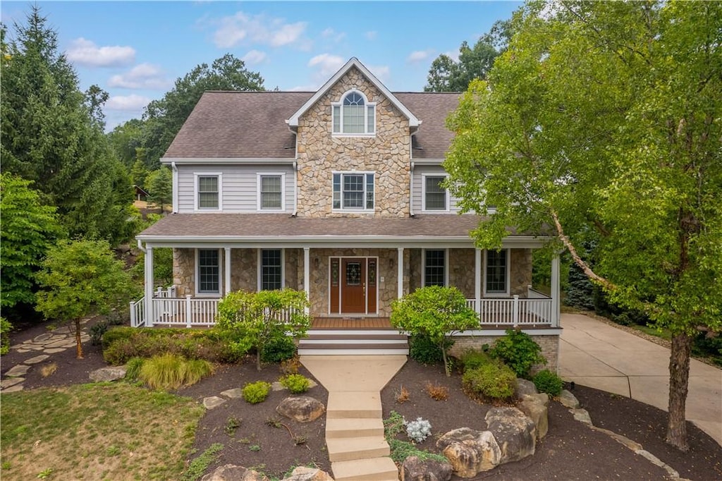 view of front of property featuring a shingled roof, stone siding, covered porch, and concrete driveway