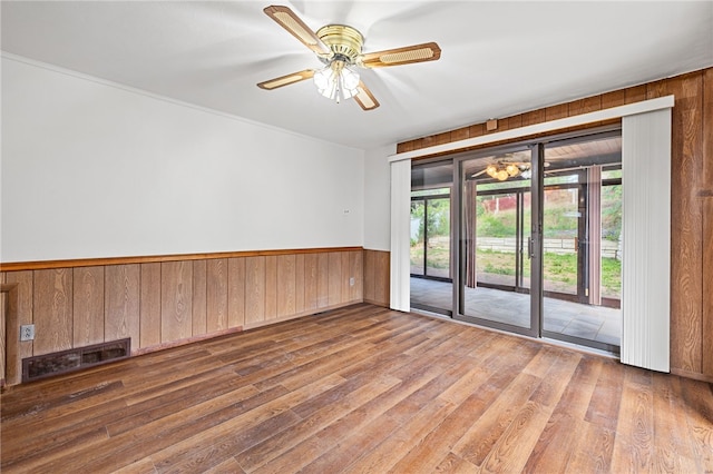 empty room featuring ceiling fan, wood walls, and wood-type flooring