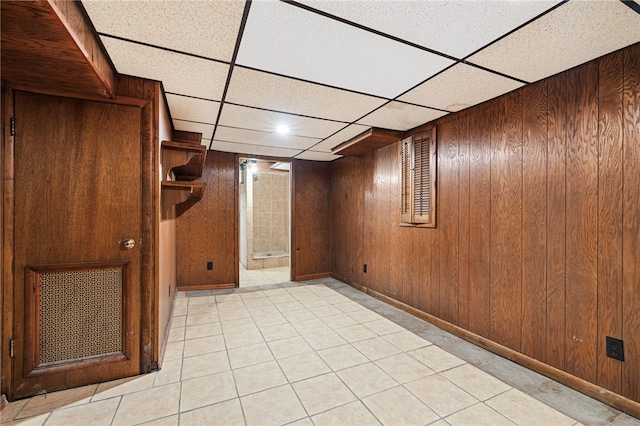 basement featuring wood walls, a drop ceiling, and light tile patterned flooring