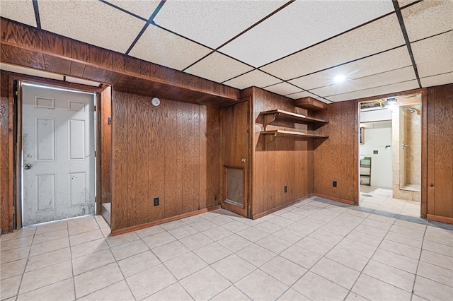 basement featuring wooden walls, light tile patterned floors, and a drop ceiling