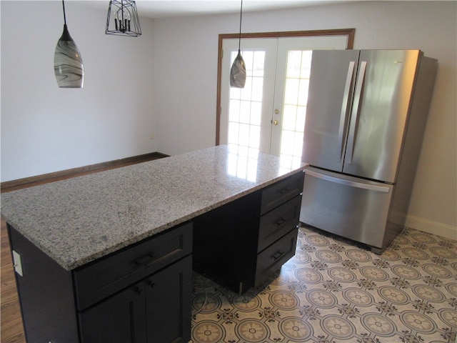 kitchen with light stone countertops, a center island, hanging light fixtures, and stainless steel fridge