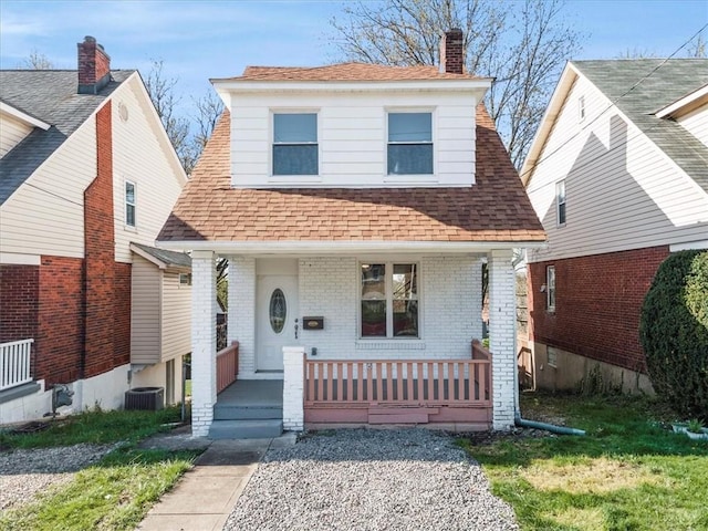 view of front facade with a chimney, roof with shingles, central air condition unit, a porch, and brick siding